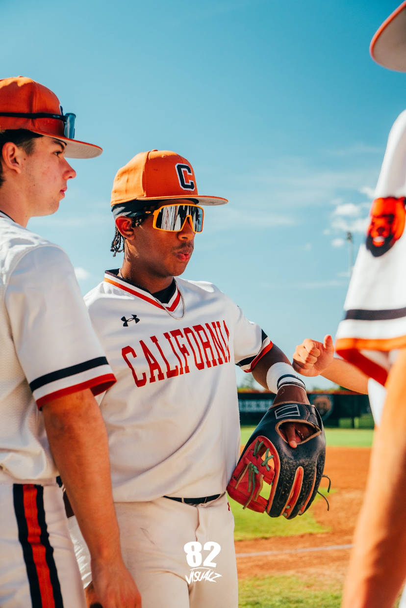 Kai Watts in the white California uniform and orange cap, fist-bumping a teammate