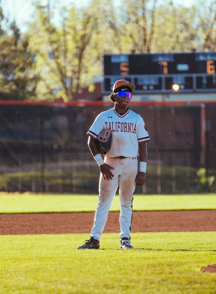 Kai Watts standing on the infield in the white California uniform, glove tucked under his arm