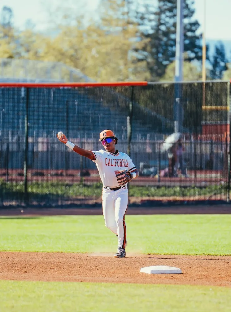 Kai Watts making a throw from the middle infield next to second base, in the white California home uniform