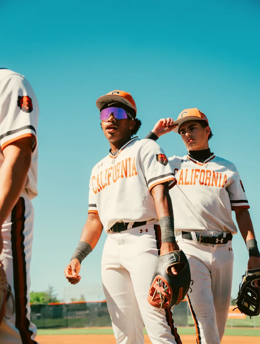 Kai Watts walking off the field with a teammate between innings, both in white California uniforms